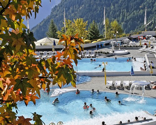 An outdoor swimming pool with chaise lounge chairs alongside mountains.