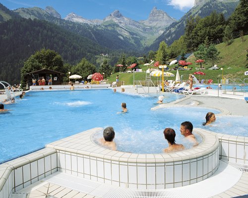 An outdoor hot tub with chaise lounge chairs surrounded by mountains.
