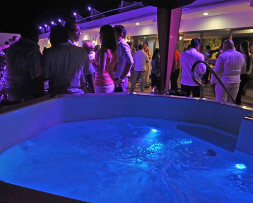 A group of people enjoying party alongside a hot tub at night.