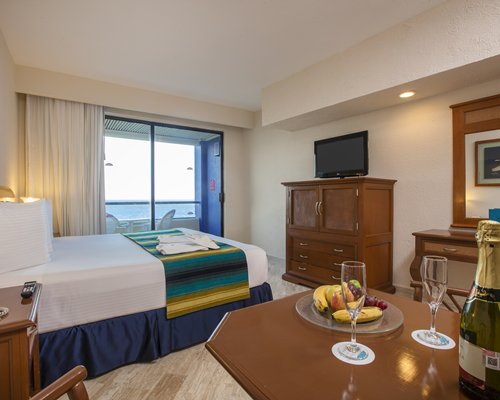 A well furnished bedroom with king bed television dining area balcony and ocean view.