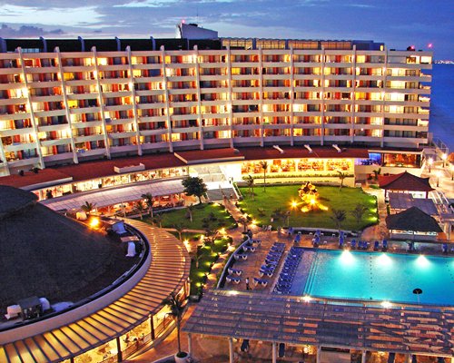 A scenic outdoor swimming pool with chaise lounge chairs alongside multi story units at dusk.