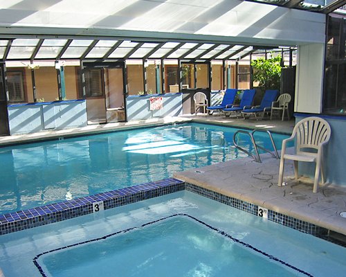 An indoor swimming pool with a hot tub and chaise lounge chairs.