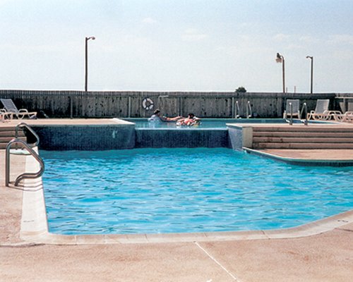 View of people at an outdoor swimming pool with chaise lounge chairs.