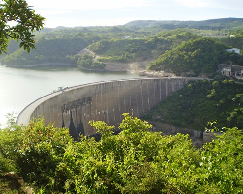 An aerial view of the dam with reservoir surrounded by wooded area.