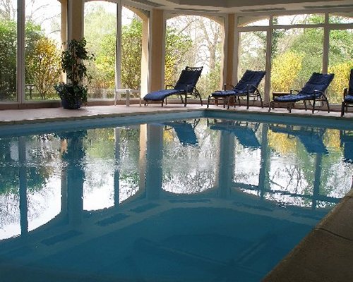 A large indoor swimming pool with chaise lounge chairs and an outside view.