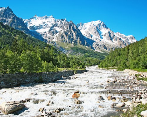 A stream surrounded by a wooded area alongside a snowy mountain.
