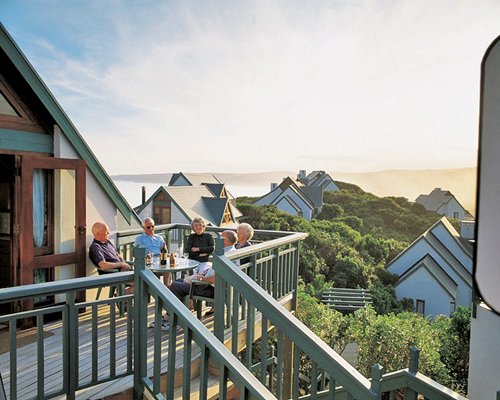 A group of people sitting on a wooden deck with a view of the ocean at sunset.