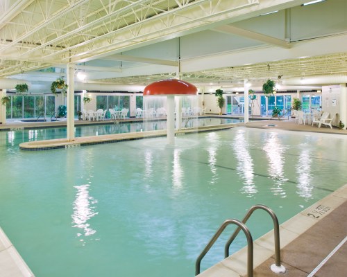 LARGE INDOOR SWIMMING POOL WITH CHAISE LOUNGE CHAIRS AND MUSHROOM UMBRELLA FOUNTAIN.
