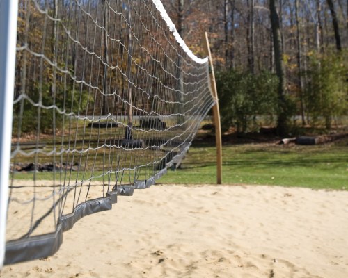 OUTDOOR RECREATION AREA WITH VOLLEYBALL NET SURROUNDED BY WOODED AREA.