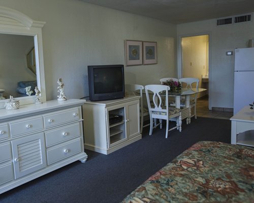 An open plan bedroom and dining area with a television and a dresser.