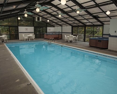 An indoor swimming pool with hot tub and patio furniture.