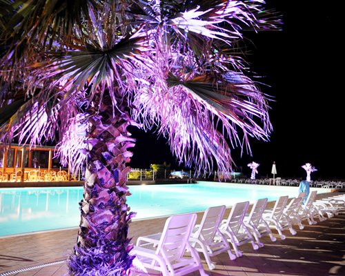 Large outdoor swimming pool with chaise lounge chairs at night.