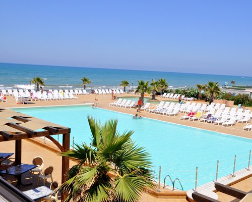 A large outdoor swimming pool with chaise lounge chairs alongside the beach.