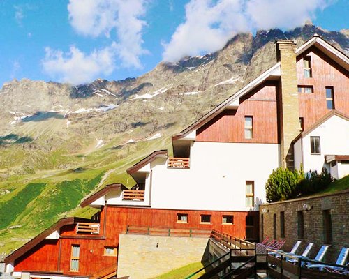 An exterior view of the Residence Cervinia 2 resort unit with chaise lounge chairs alongside a hill.