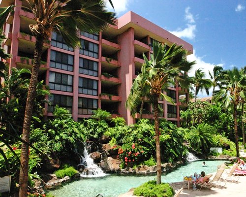 A scenic outdoor swimming pool with waterfall and chaise lounge chairs alongside the resort.