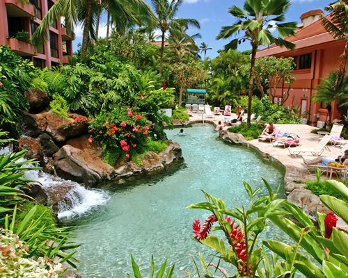 Scenic outdoor swimming pool with fountain chaise lounge chairs alongside multi story resort units.