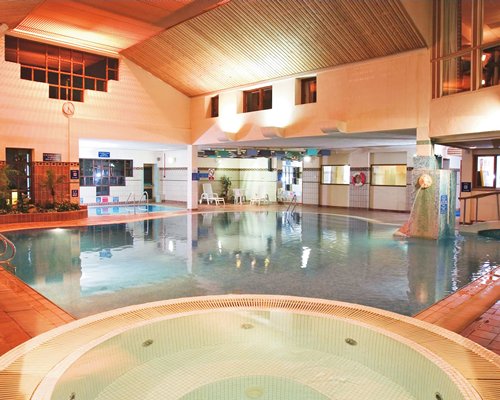 An indoor swimming pool with hot tub and chaise lounge chair.