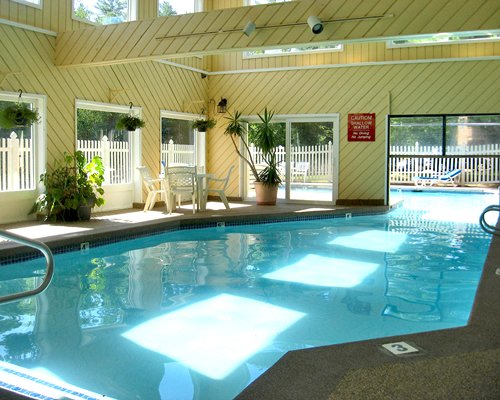 Indoor swimming pool with patio furniture and chaise lounge chair.