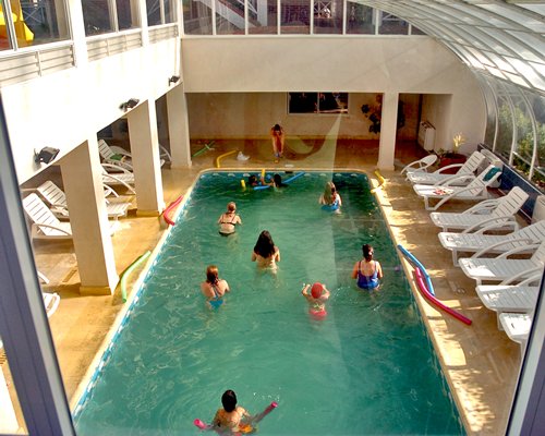 An indoor swimming pool with chaise lounge chairs with an outside view.