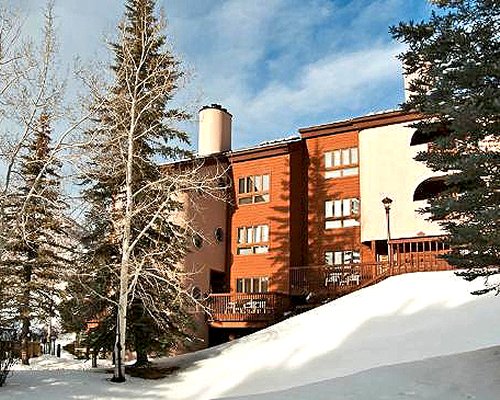 An exterior view of the RHC/Streamside At Vail Cedar resort covered in snow alongside pine trees.