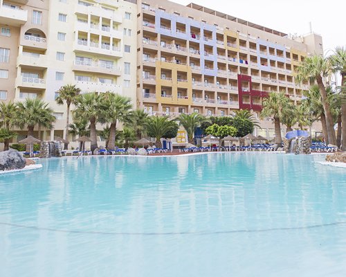 A large outdoor swimming pool with chaise lounge chairs alongside multi story resort units.