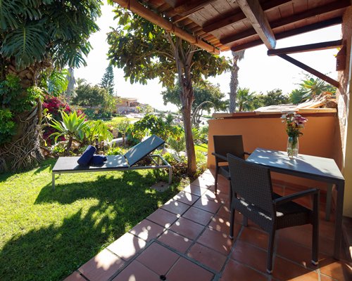 An outdoor porch with table chaise lounge chair and garden view.