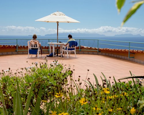 An open terrace with couple at table under umbrella overlooking water view.