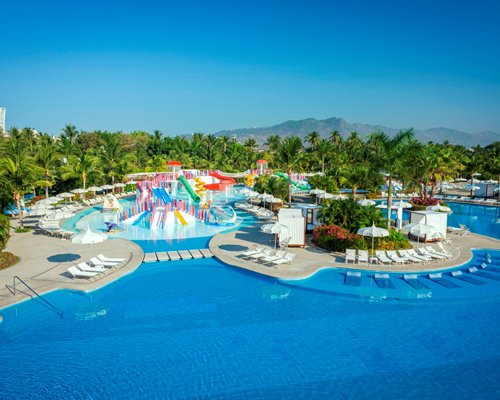 Large outdoor swimming pool with water theme park chaise lounge chairs surrounded by wooded area.