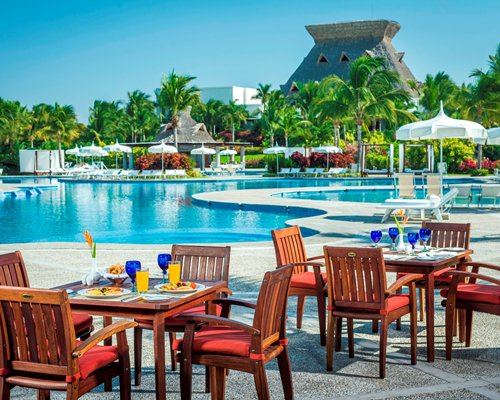 Outdoor poolside restaurant with chaise lounge chairs and sunshades.