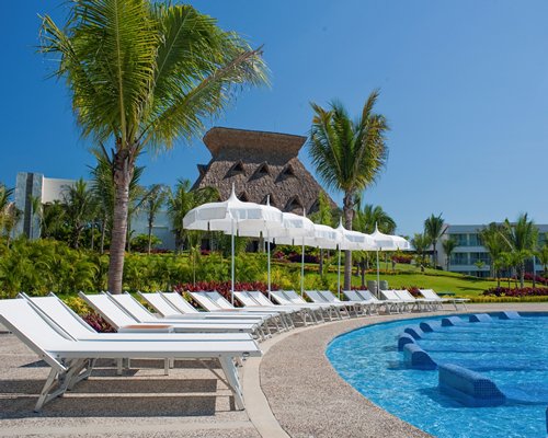 Outdoor swimming pool with chaise lounge chairs sunshades and thatched sunshade.