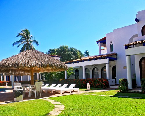 Scenic view of a resort condo with chaise lounge chairs and thatched sunshades.