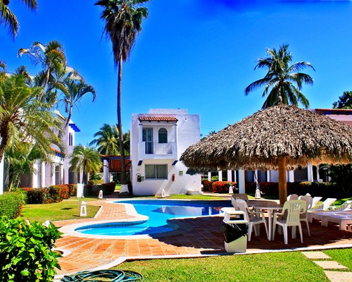 Outdoor swimming pool with chaise lounge chairs thatched sunshade and palm trees.