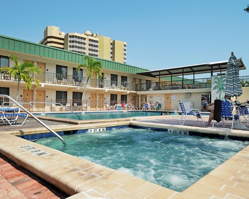 Exterior view of outdoor swimming pool and hot tub with chaise lounge chairs alongside resort.