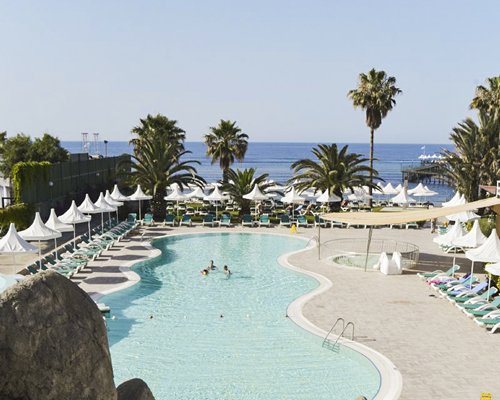 An outdoor swimming pool with chaise lounge chairs and thatched sunshades.