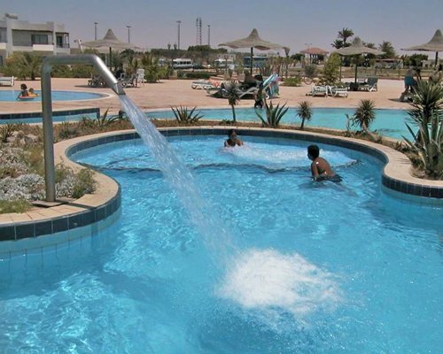 View of multiple outdoor swimming pools with chaise lounge chairs and sunshades.