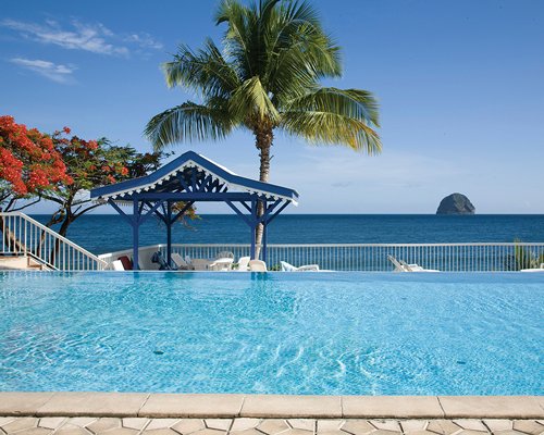 An outdoor swimming pool with chaise lounge chairs alongside the ocean.