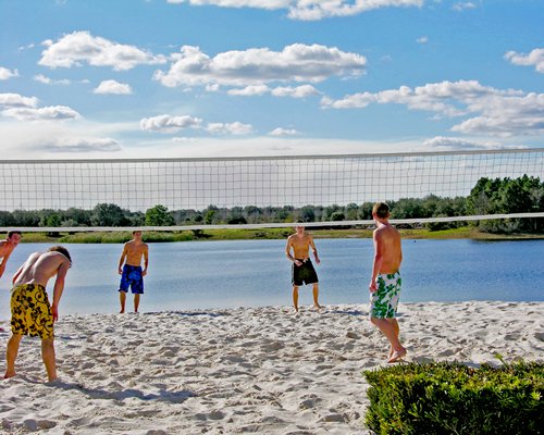 View of people at outdoor volleyball court alongside lake.