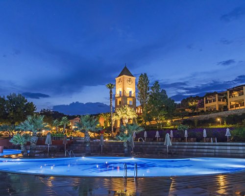 An outdoor pool with chaise lounge chairs alongside resort condos at dusk.