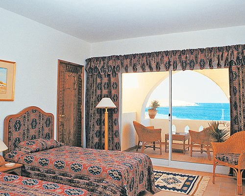 A well furnished bedroom with two twin beds balcony having patio furniture and sea view.