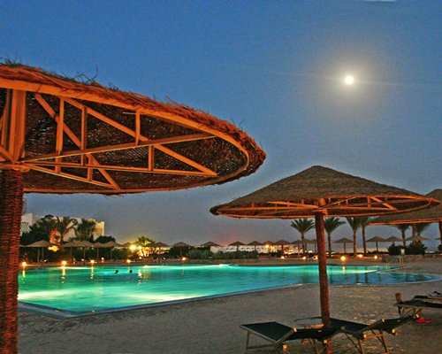 Outdoor swimming pool with chaise lounge chairs and thatched sunshades.
