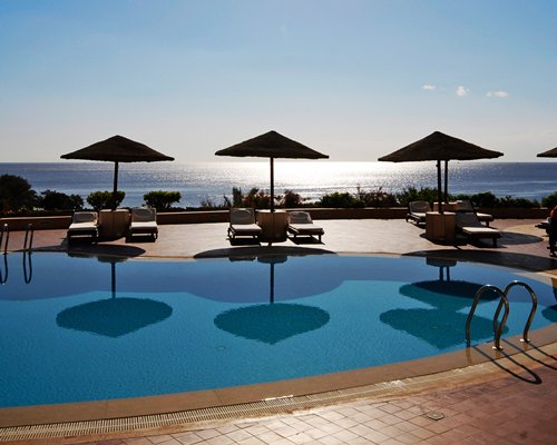 Outdoor swimming pool with chaise lounge chairs and sunshades alongside the sea.
