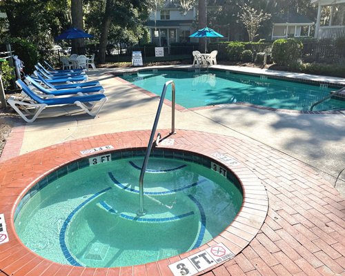An outdoor swimming pool with patio chairs and umbrella alongside resort condo.