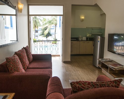 A well furnished living room with a television alongside a kitchen and an outside view.