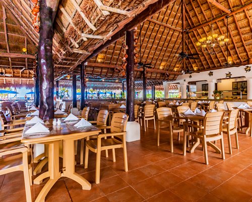 Open-air restaurant with tables, high thatched ceiling and ocean view.