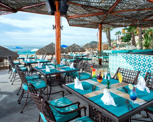 An outdoor fine dining area with thatched sunshades alongside the beach.