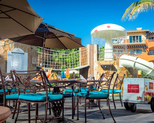 Outdoor restaurant with sunshades alongside children's theme park.