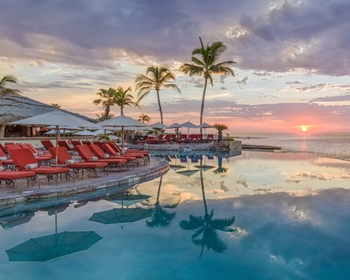 An outdoor swimming pool with chaise lounge chairs facing the ocean.