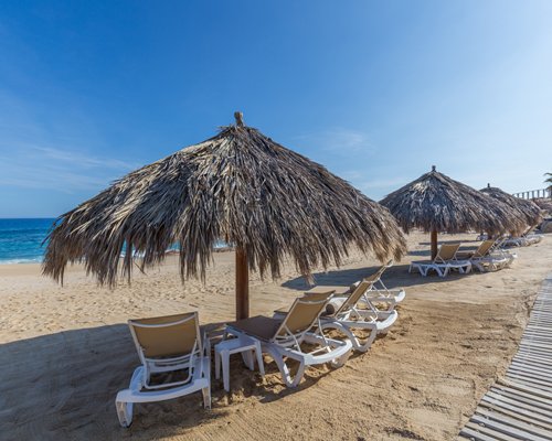 A beach view of chaise lounge chairs under a sunshade facing the ocean.