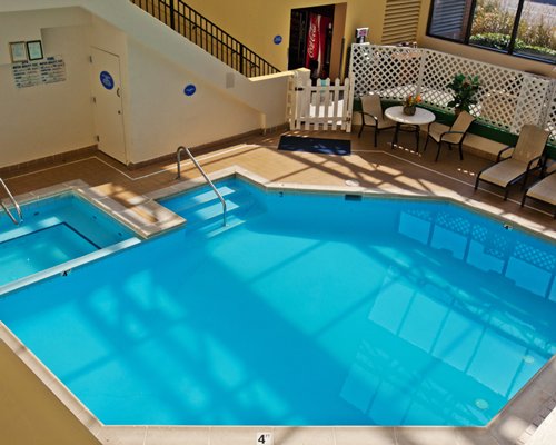 An indoor swimming pool and hot tub with chaise lounge chairs.