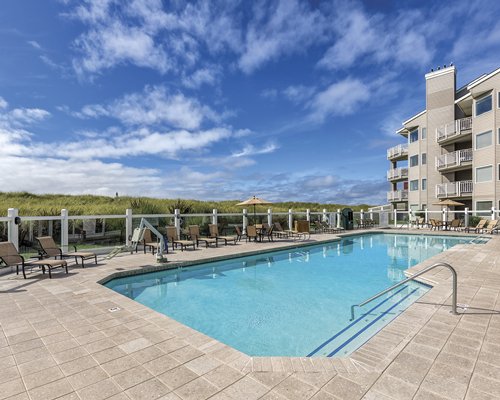 An outdoor swimming pool with chaise lounge chairs alongside multi story resort condos.